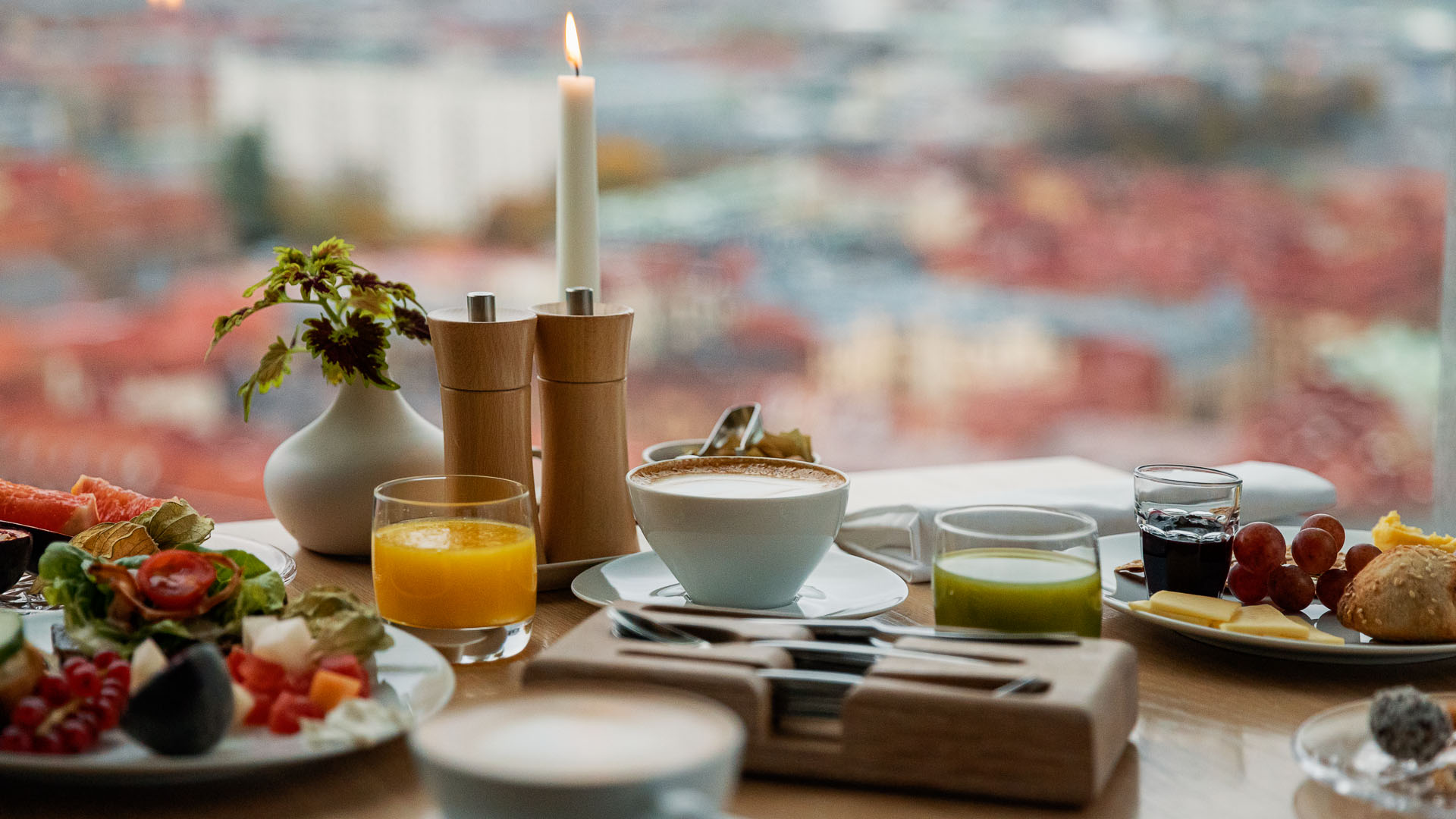 En hotellfrukost med färsk juice, yoghurt, bröd, frukt och ett tänt ljus på bordet med utsikt över Göteborg i bakgrunden.